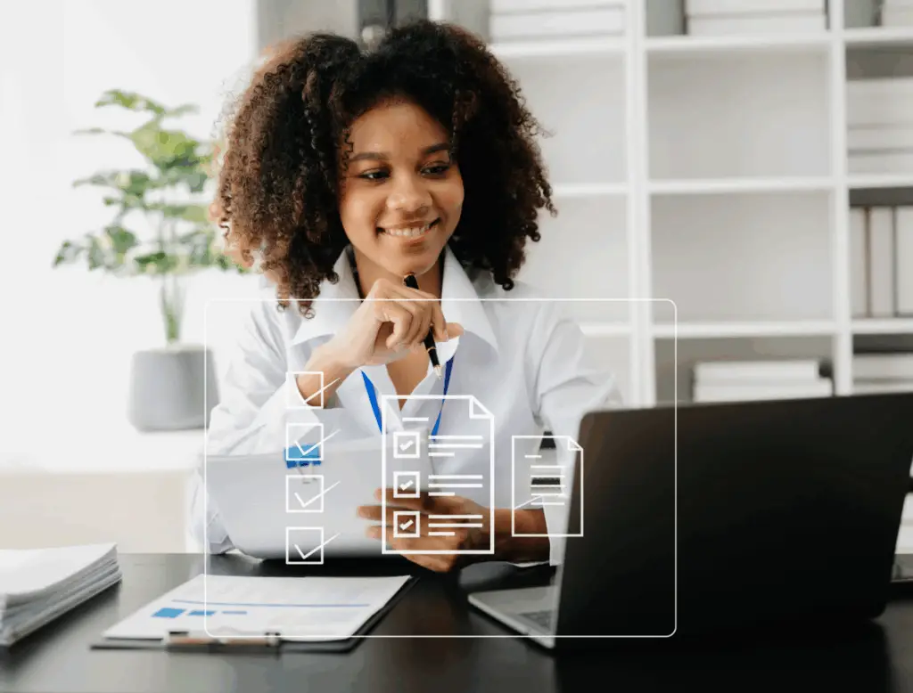 Smiling woman holding a pen and looking at computer monitor while managing leave compliance with BlueJLeaves software